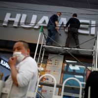 Workers wearing face masks fix the logo of Chinese electronics manufacturer Huawei at a mobile phone store in Beijing on April 24. | REUTERS