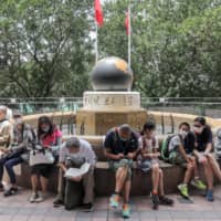 People sit outside the Central Library in the Causeway Bay district of Hong Kong, China, on May 6 after the city\'s leader, Carrie Lam, moved to loosen curbs on social gatherings and reopen shuttered schools. | BLOOMBERG