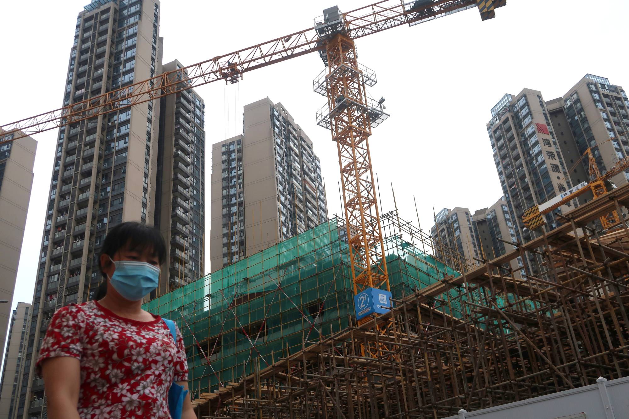 A woman wearing a face mask walks past a construction site near residential buildings in Shenzhen on Sunday. | REUTERS