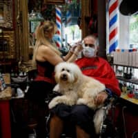 A hairdresser wearing a protective mask cuts the hair of a man at a barber shop, as Miami-Dade County eases some of the lockdown measures put in place during the coronavirus disease outbreak, in Miami on Monday. | REUTERS