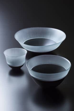 Patina: From photo top, this deep dish (18.5 x 7 centimeters), sake cup (7.5 x 6 centimeters) and bowl (13 x 6 centimeters) with black base and silk-thread pattern, ¥50,000 each, are by Masao Adachi. Applying an original technique, Adachi mixes a special blend of materials to produce the black glass, which he builds up in multiple layers while firing each in turn. The result is a rare vessel that changes its appearance over time, acquiring more luster the more it is used. | 