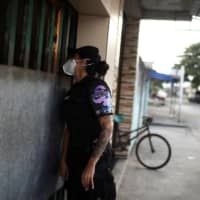 A police officer waits outside the house of a woman who was a victim of domestic violence, to ensure that she is not in danger, amid the COVID-19 outbreak in Rio de Janeiro last month. | REUTERS