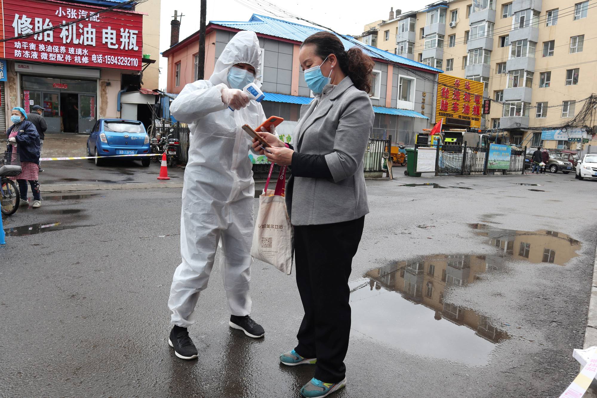 A worker in protective suit takes the body temperature measurement of a woman following the coronavirus disease outbreak in Jilin, in China's Jilin province, on Sunday.  | CNSPHOTO / VIA REUTERS