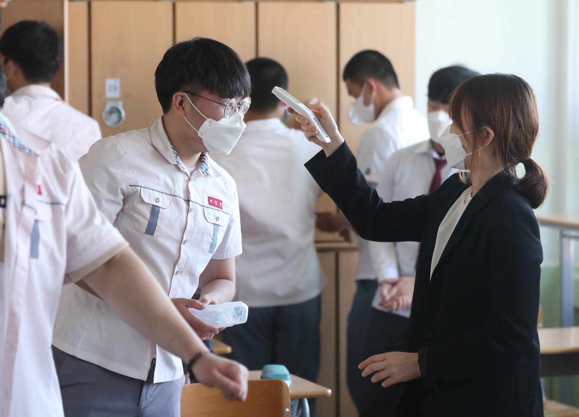 A high school teacher checks the temperature of a student in Gimhae, South Korea, on Wednesday.  | YONHAP / VIA REUTERS