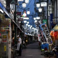 A restaurant worker stands in a nearly empty street in the Kamata district of Tokyo on Friday night. | BLOOMBERG