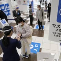 Customers have their temperatures checked at an entrance of the Seibu department store in Tokyo\'s Ikebukuro district on Saturday.  | KYODO