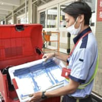 A post office worker delivers so-called Abenomasks to households in the city of Fukui on Saturday. | KYODO
