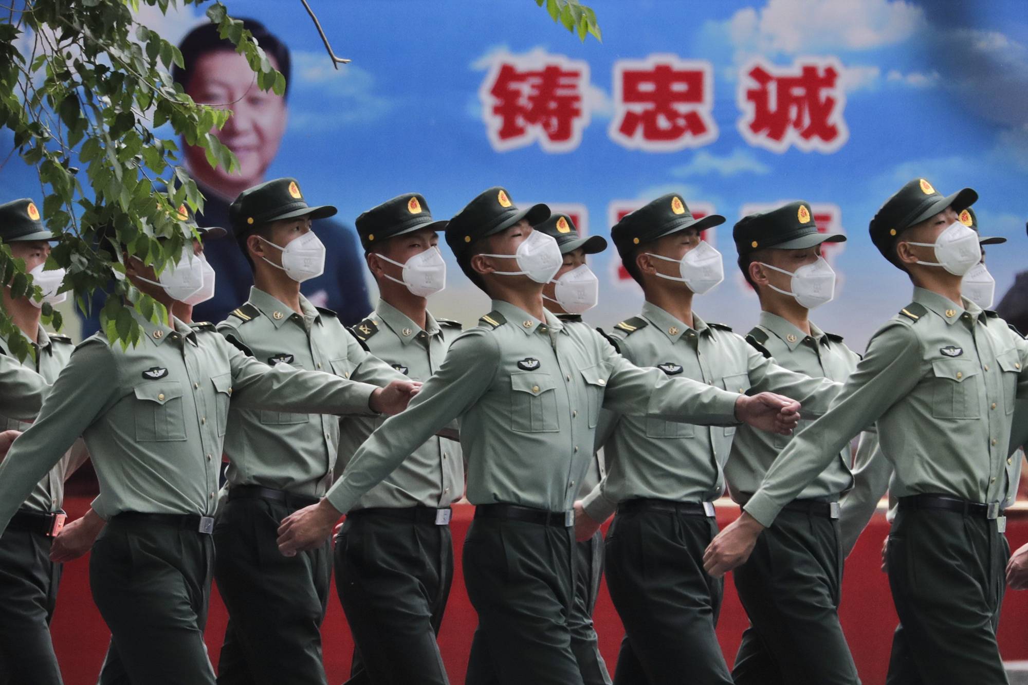 Chinese People's Liberation Army soldiers  march past a banner depicting Chinese President Xi Jinping inside the Tiananmen Gate in Beijing during a plenary session of China's National People's Congress at the Great Hall of the People on Monday. | AP