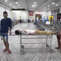 Indian attendants wait to register a man suffering from fever before a swab test for coronavirus in Guwahati Medical College Hospital in Gauhati, India, on May 17. | AP