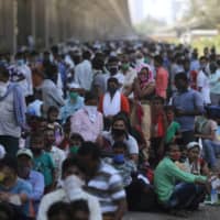 Migrants wait along a road for transportation to a railway station during an extended lockdown to slow the spread of the coronavirus in Mumbai on Friday.  | REUTERS 
