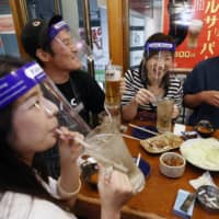 Customers wearing face shields enjoy drinking at a pub in Osaka on Monday night. | KYODO