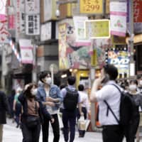 Pedestrians wearing protective masks walk through a shopping district in the Kichijoji district of Tokyo on Tuesday, a day after the government ended the state of emergency nationwide. | BLOOMBERG