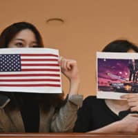 Two women hold up posters of the U.S. flag and a depiction of President Donald Trump during a rally in a shopping mall in Hong Kong on Thursday. | AFP-JIJI