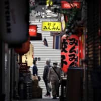 Pedestrians wearing protective masks walk through a shopping street in the Kichijoji area of Tokyo on Tuesday.  | BLOOMBERG