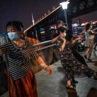 People wearing face masks dance in a park next to the Yangtze River in Wuhan, China, on Wednesday. | AFP-JIJI