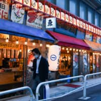 A pedestrian wearing a protective mask walks past a traditional Japanese pub in the Yurakucho district of Tokyo on Friday.
 | BLOOMBERG
