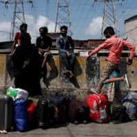 A boy jumps over luggage as people wait for transportation to a railway station during an extended lockdown to slow the spread of the coronavirus in Mumbai on Thursday. | REUTERS
