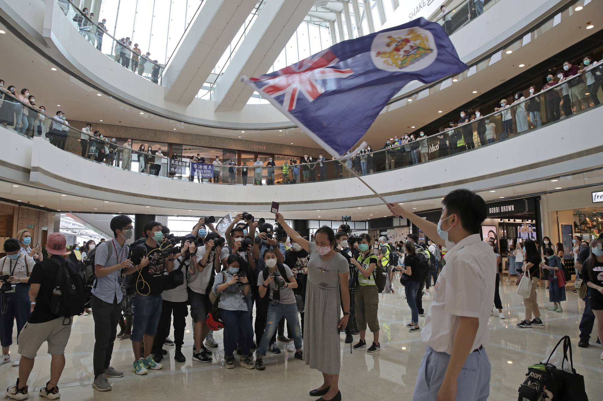 Protesters in Hong Kong hold a British National (Overseas) passport and Hong Kong colonial flag in a shopping mall during a protest against China's national security legislation for the city on Friday.  | AP