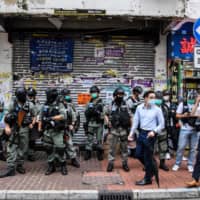 Pedestrians walk past a group of riot police standing guard in a front of a shop in the Causeway Bay district of Hong Kong on Wednesday. | AFP-JIJI