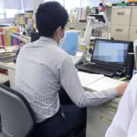A worker receives a call at a public health center in Fujisawa, Kanagawa Prefecture, earlier this month. The computer screen is blurred for privacy reasons. | KYODO