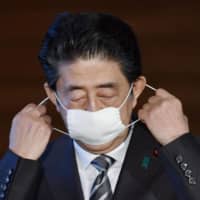 Prime Minister Shinzo Abe takes off his mask during a news conference Friday at his office. | KYODO