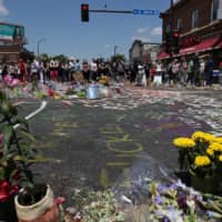 People gather at a memorial for George Floyd that has been created at the place where he was taken into police custody and later died in Minneapolis on Monday. | REUTERS