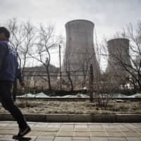 A man walks past cooling towers at the Beijing Jingneng Power Co. Thermal Power Plant in Beijing in 2016. | BLOOMBERG