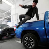 A worker jumps off a Toyota Tundra pickup truck at Pickup Fan Club, on the outskirts of Beijing. | REUTERS
