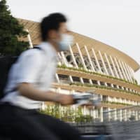 A man rides past the National Stadium in Tokyo, the main venue of the delayed Olympics and Paralympics, on Thursday. | KYODO