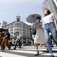 People walk under a strong sun in Tokyo\'s Ginza shopping area on Tuesday, wearing face masks amid continued worries about the novel coronavirus. | KYODO