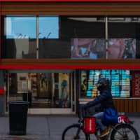 A Grubhub delivery worker passes by a Famous Footwear store in New York\'s Herald Square area on May 12. | BLOOMBERG