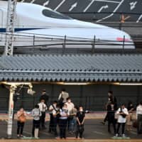 People wearing face masks wait for local trains while a Shinkansen passes JR Shimbashi Station in Tokyo on Wednesday. | AFP-JIJI