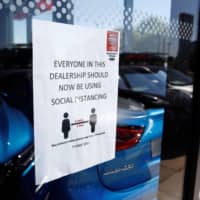 A social distancing sign is seen at a Nissan car dealership in Northwich, England, last month. | REUTERS