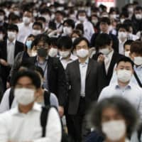 People commute in Tokyo on June 5. Researchers have found that death rates were lower in countries like Japan that have a combination of high government efficiency and high cultural “tightness” — strong norms and a pressure for conformance. | AP