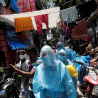 Health care workers and volunteers walk through the Dharavi slum in Mumbai on June 7.  | REUTERS
