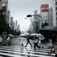 Pedestrians cross a street in the Shinjuku district of Tokyo on Sunday. | BLOOMBERG