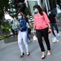 People with protective masks walk with take away food at the Raffles Place financial business district in Singapore on Monday. | AFP-JIJI