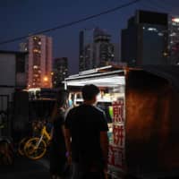 People buy food from a street vendor near a subway exit in Beijing on June 10. | AFP-JIJI