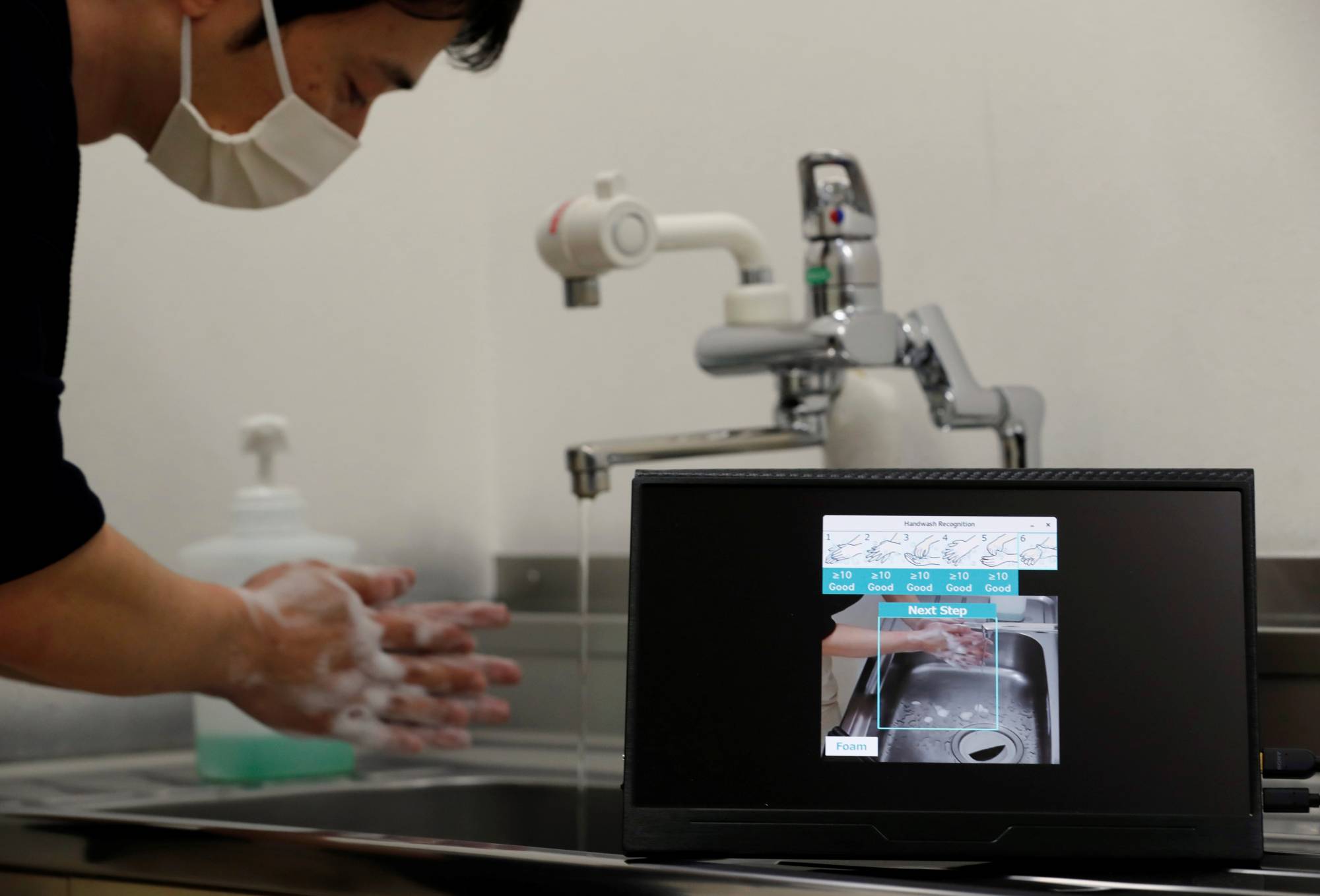 Fujitsu senior researcher Genta Suzuki washes his hands as he demonstrates AI-based recognition technology that checks whether people follow the six hand-washing steps recommended by the health ministry, during an interview at the company's research and development laboratory in Kawasaki on Wednesday. | REUTERS