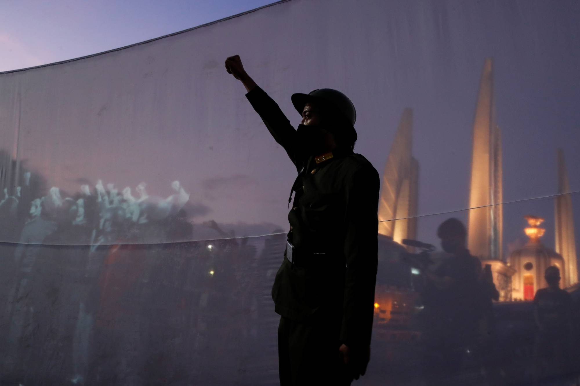 A demonstrator dressed in a vintage uniform raises his fist next to images of the 1932 coup in Thailand, in Bangkok on Wednesday. | REUTERS