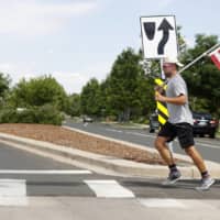 A runner carries an American flag while crossing a street in Denver on Monday. | AP