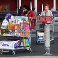 People leave a Costco outlet with a trolley full of toilet paper and cleaning products as fears of a second wave of COVID-19 have sparked a rush on some supermarket items in Melbourne.  | AFP-JIJI