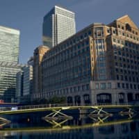 Pedestrians cross a footbridge in view of buildings in the West India Dock in the Canary Wharf financial district in London. | BLOOMBERG