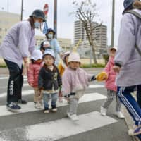 Preschool teachers carefully guide children at a crosswalk in Osaka in February.   | KYODO
