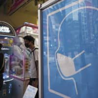 A sign to wear a protective mask to help curb the spread of the new coronavirus is seen at the entrance to a game center in Tokyo on Friday. | AP