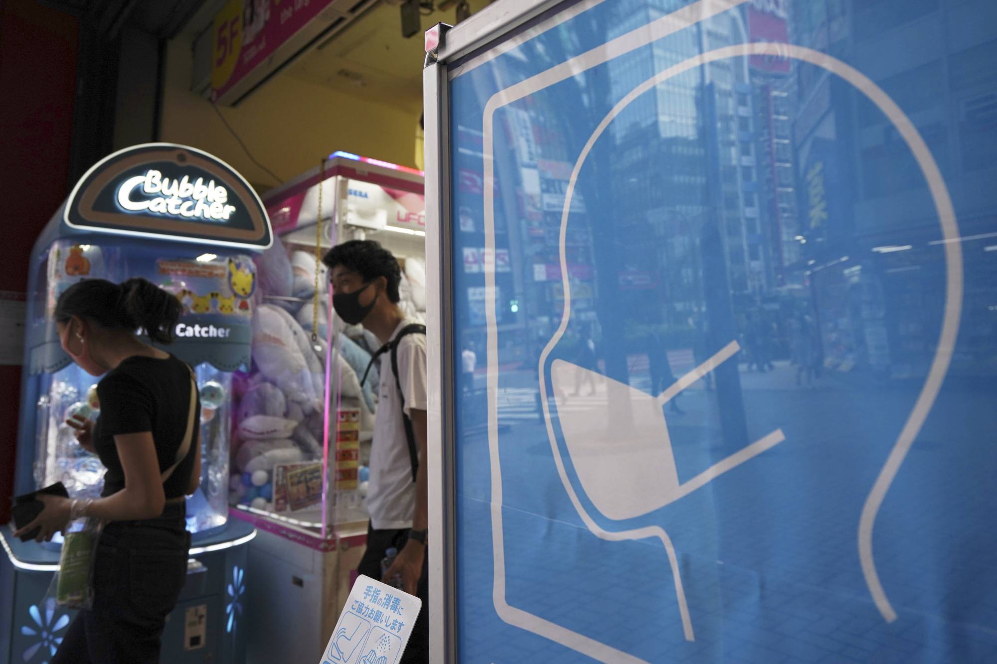 A sign to wear a protective mask to help curb the spread of the new coronavirus is seen at the entrance to a game center in Tokyo on Friday. | AP