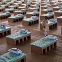 A volunteer walks past disposable beds made out of cardboard on Friday at the campus of Radha Soami Satsang Beas, a spiritual organization, in New Delhi, where a coronavirus care center has been constructed for patients amid the pandemic. | REUTERS