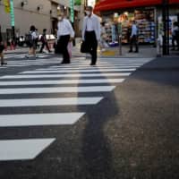 Pedestrians wearing protective masks make their way through downtown Tokyo on Monday. | REUTERS