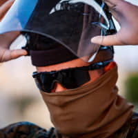 A U.S. Marine dons personal protective equipment (PPE) to begin screening incoming personnel in response to the increased threat of COVID-19 at Camp Foster, in Okinawa Prefecture, in April 10. | U.S. MARINE CORPS / VIA REUTERS