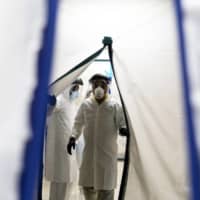 A doctor wearing protective gear goes through an air tight curtain while entering the COVID-19 intensive care unit at the United Memorial Medical Center in Houston, Texas, on Monday. Japanese pharmaceutical firm Eisai Co. is set to start clinical trials in the United States of its experimental drug eritoran in the battle against coronavirus. | BLOOMBERG